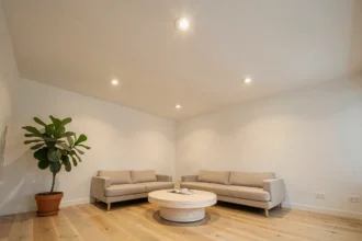 Plafond de salon moderne avec ampoules spot encastrables LED intégrées dans du plâtre blanc, sol en chêne clair et décoration scandinave minimaliste