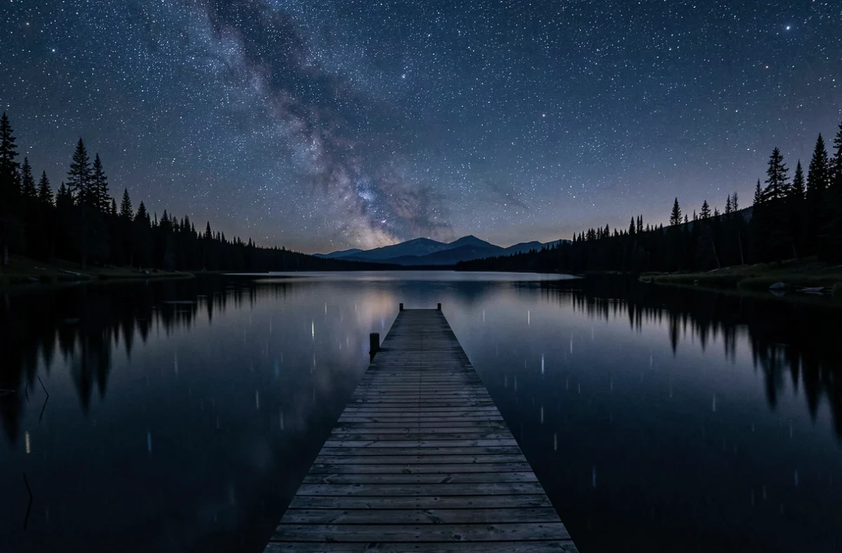 Un ponton en bois sur un lac calme sous un ciel nocturne profondément bleu foncé étoilé